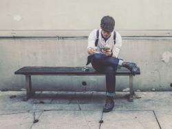 Junger Mann mit Zigarette und Handy auf einer Bank